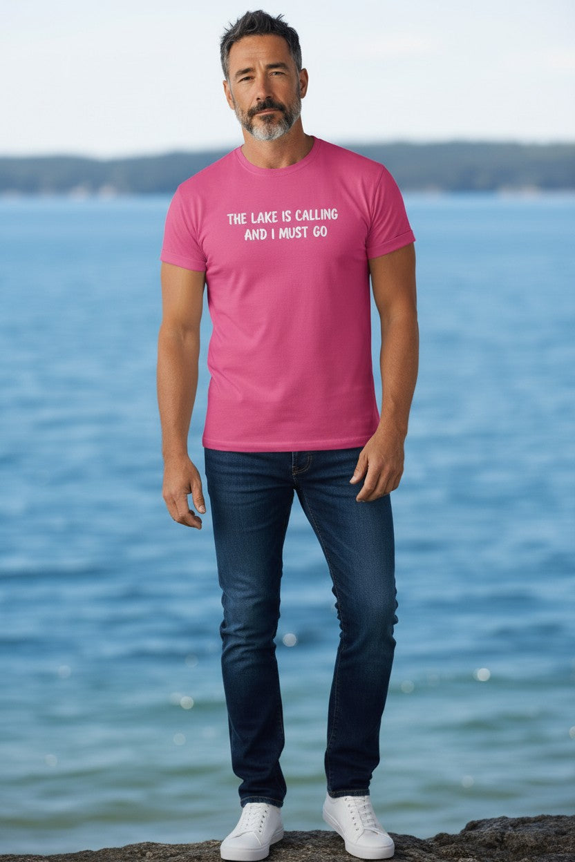 Man wearing a pink Lakelifewear T-shirt with The Lake Is Calling and I Must Go text, standing by the water.