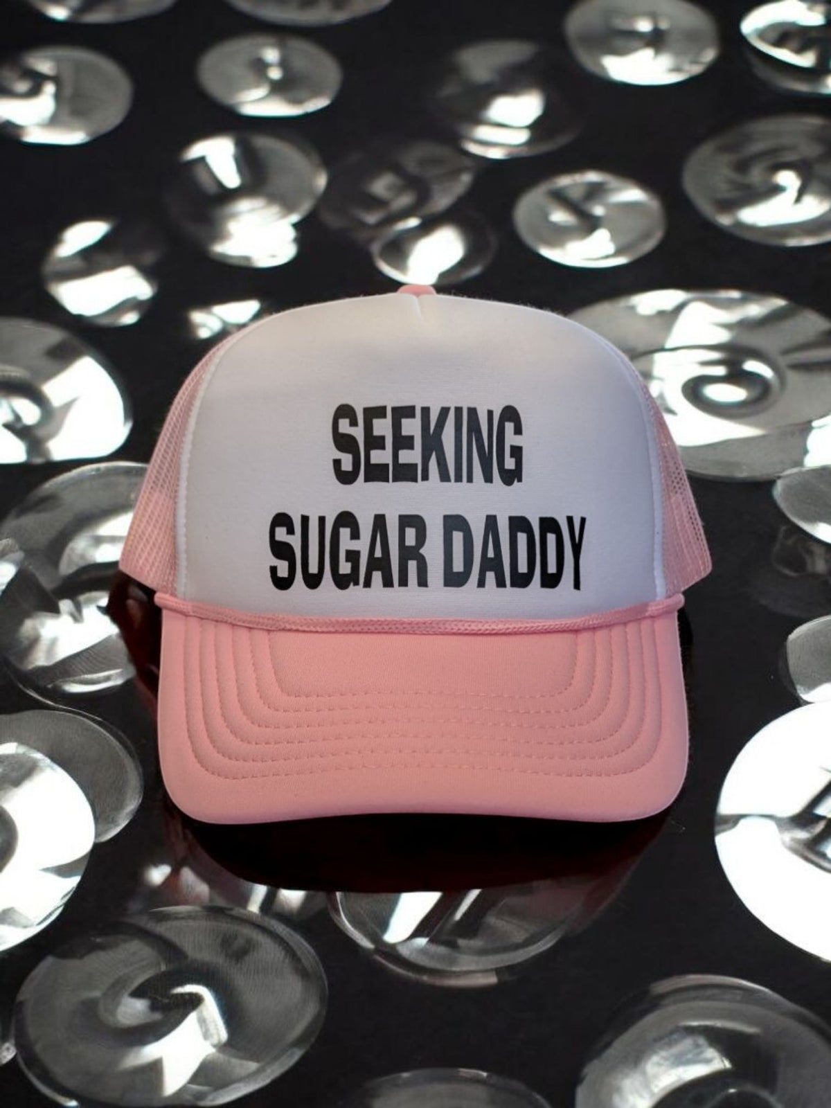 Lakelifewear pink and white foam trucker hat with Seeking Sugar Daddy slogan and rope detail on a reflective surface.
