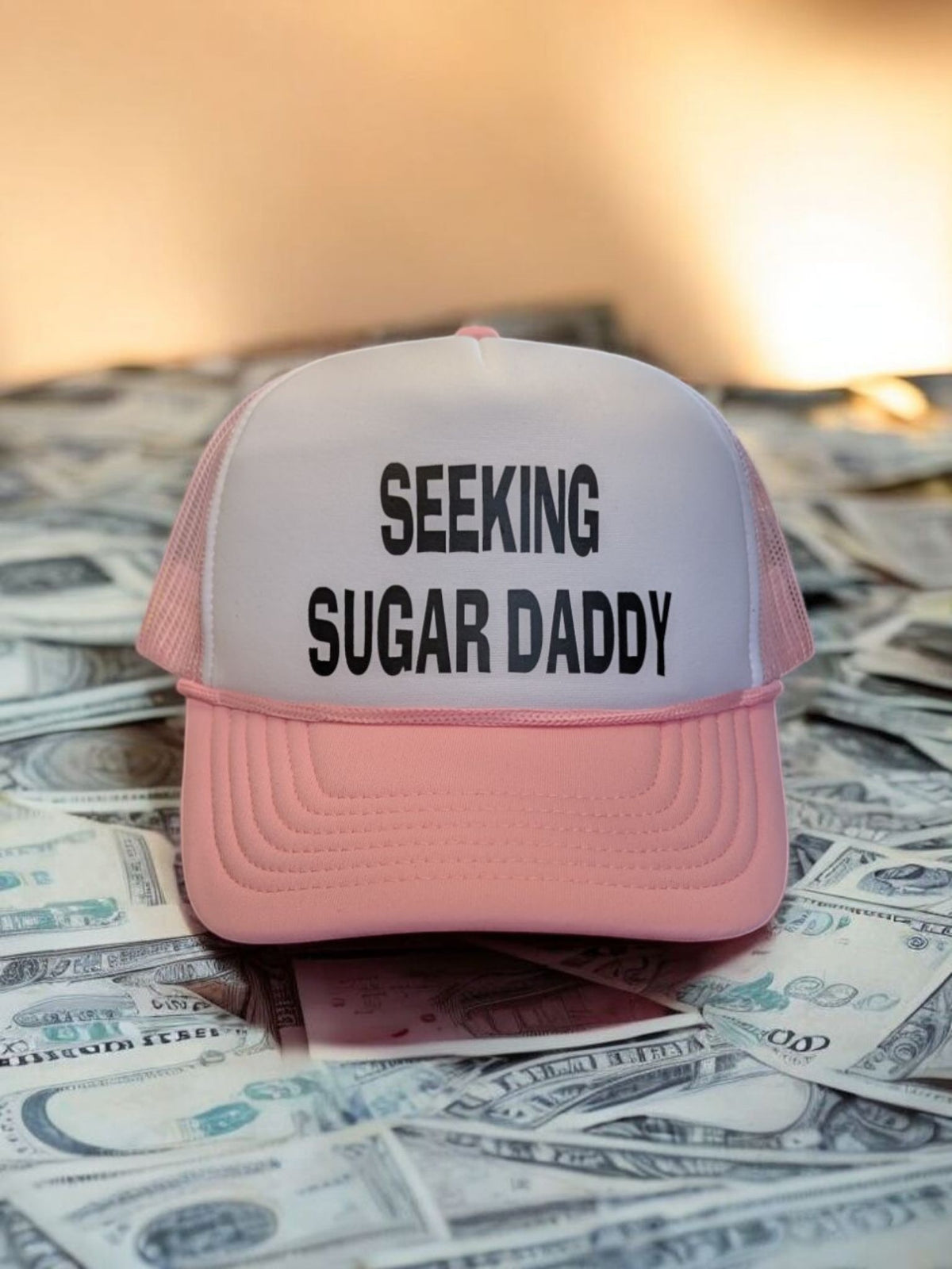 Pink and white foam trucker hat with Seeking Sugar Daddy slogan in black text on a pile of cash
