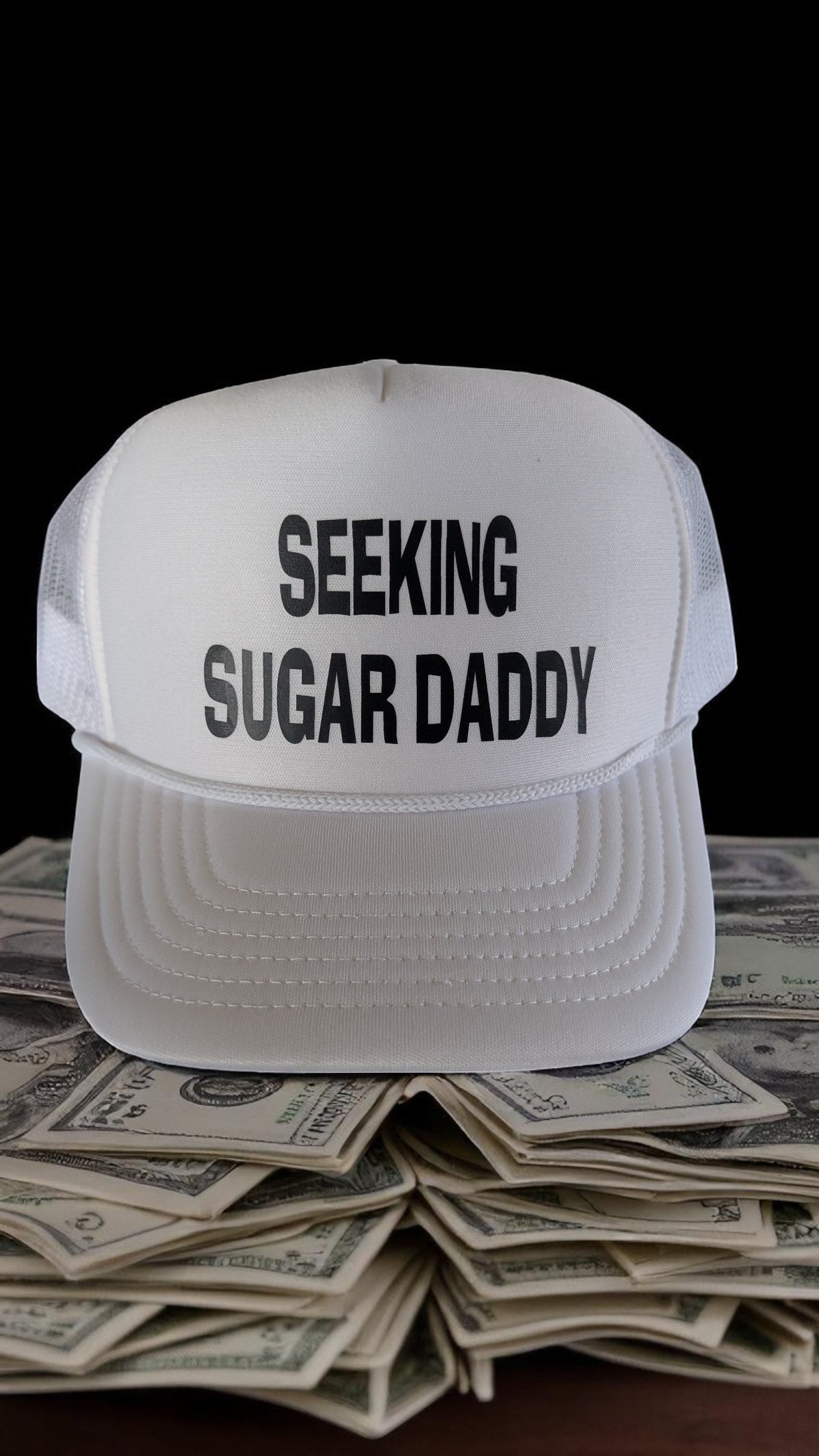 Lakelifewear white foam trucker hat with rope detail and black Seeking Sugar Daddy text resting on a stack of cash.